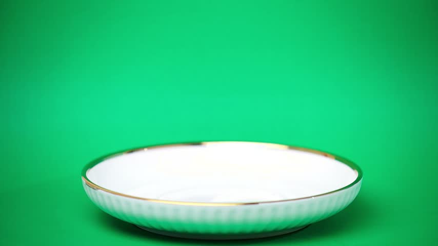 Hand stacking chocolate chip cookies on a white plate with green background