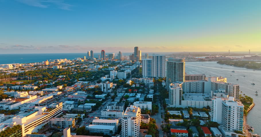 Flight above the beautiful green cityscape of Miami, Florida, USA. Setting sun lights the part of the scenery surrounded by the blue waterscape.