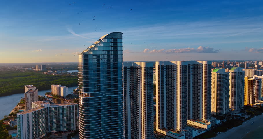 Gorgeous high-rises at the ocean shore in Miami, Florida, USA. Green scenery of coastal city at sunset from drone.