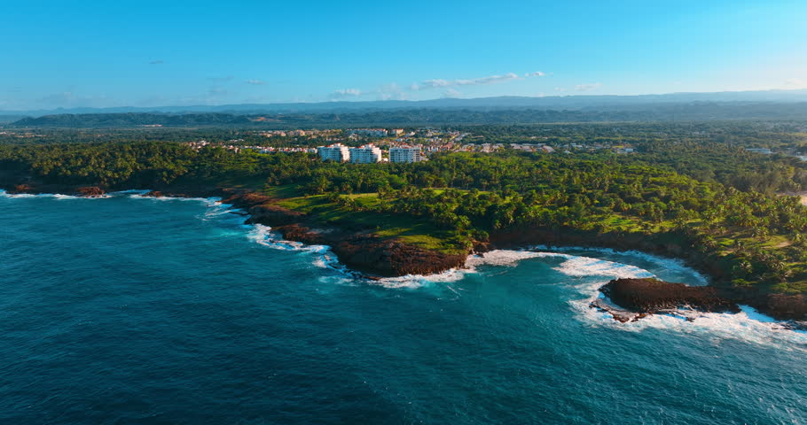 Strong waves roll to the rocky shore in Puerto Rico. Lush greenery covers the coast surrounding the cityscape.