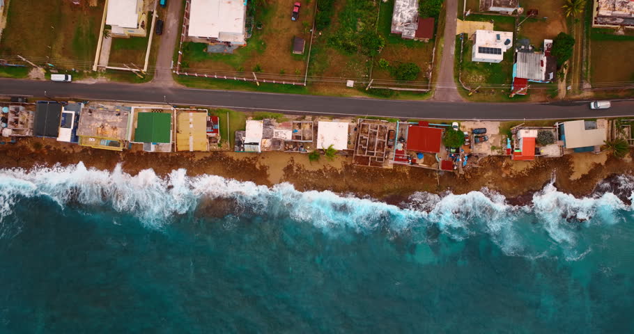 Flight over the shabby roofs of the houses located on the shore. Foamy waves splash on the narrow beach. Puerto Rico.