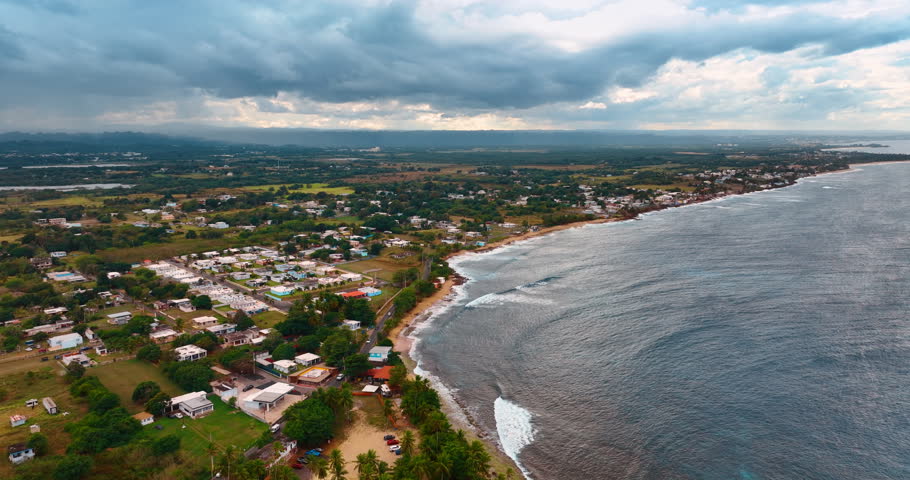 Large waves roll to the shore of Puerto Rico. Picturesque urban landscape under grey cloudscape. Aerial view.