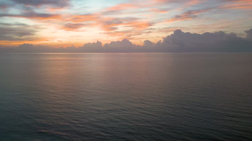 Soft pastel clouds drift above a tranquil ocean as the horizon glows with fading light off the Miami coast.