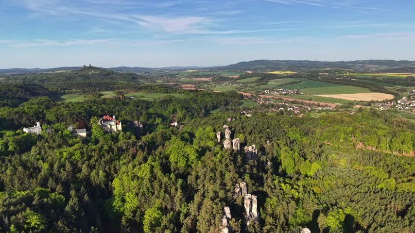Scenic aerial perspective shows weathered stone ruins on hill, treetops and canopy stretching across slopes, and patterned fields leading to distant ridgelines in calm daylight.