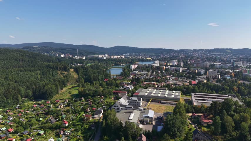 High altitude aerial panorama shows wooded hills blending into built riverfront where bridges cross water, residential blocks face shoreline.