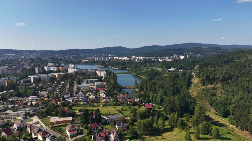 View from above showing winding river cutting through residential streets. Bridges span water beside parks and forested hills, with clear sky and bright daytime light.