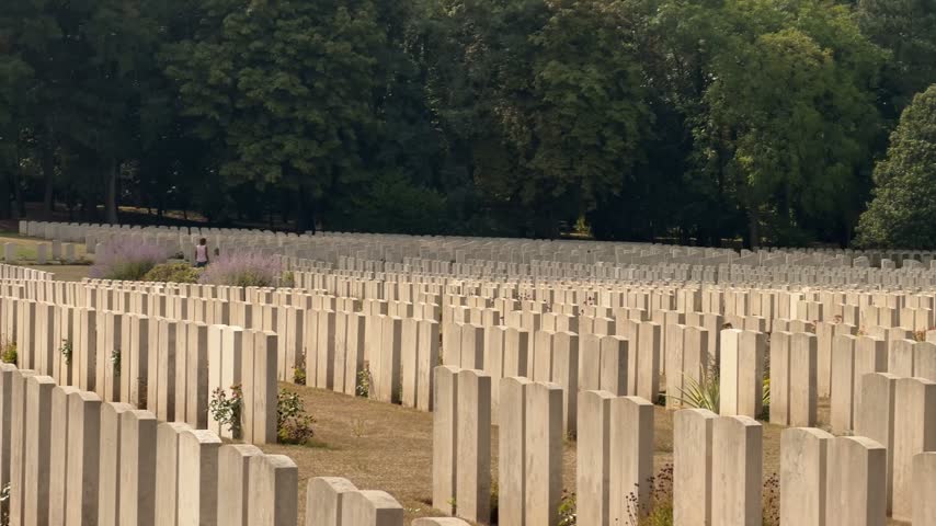 Rows of white gravestones in a large military cemetery bordered by trees in France
