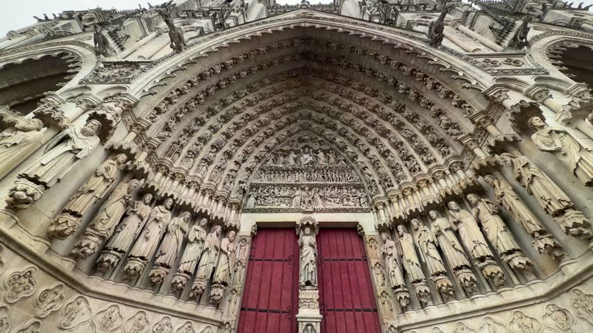 Upward view of ornate Gothic cathedral portal with detailed stone sculptures and doors