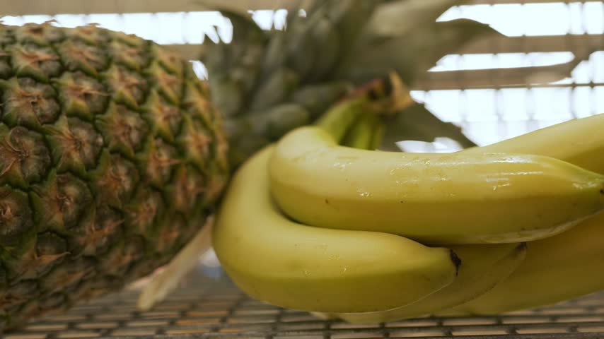 Fresh tropical fruits displayed together, featuring a ripe pineapple and a bunch of yellow bananas on a textured surface in a well-lit environment