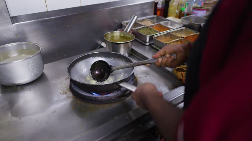 High-angle view of a chef frying ingredients with a ladle on a commercial stove.