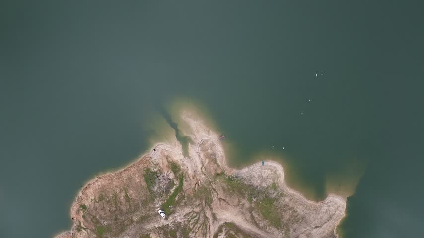Aerial view looking down at the textured shore of a teal-green lake, showing intricate inlets, rocky land, and small boats.
