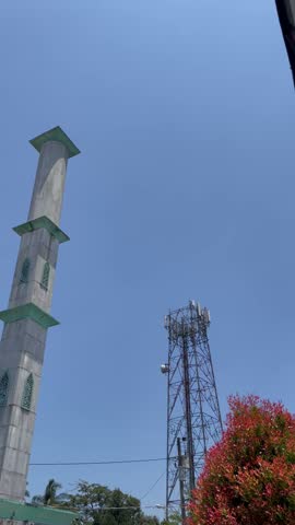 Islamic mosque tower standing beside cellular network tower under bright blue sky