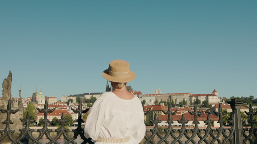 A woman in a white dress stands at Charles Bridge, viewing Prague
