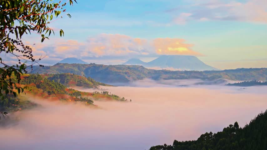 Low-lying clouds fill valleys beneath towering peaks under a soft sunrise sky.