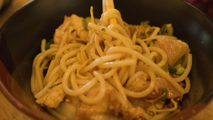 Close-up shot of chopsticks lifting flavorful Burmese Mee Shay rice noodles from a bowl.