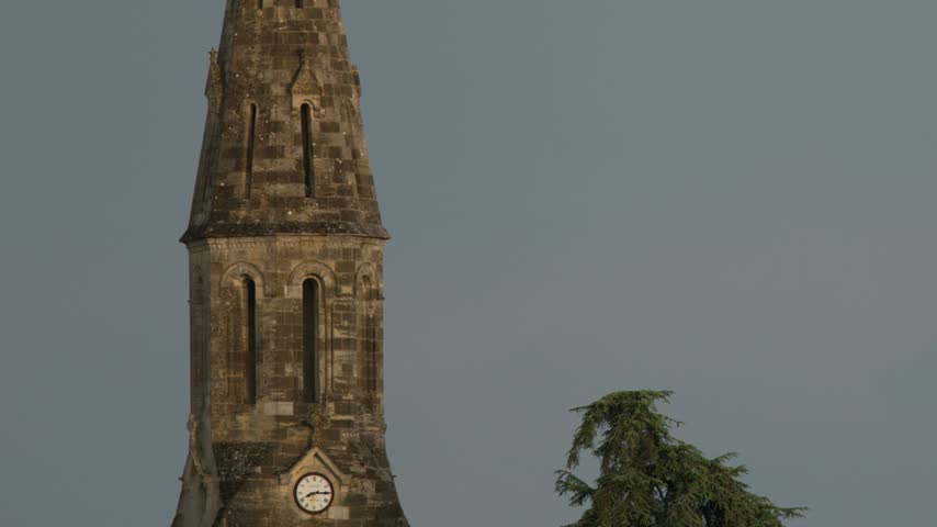 Slow tilt up a historic stone church spire against an overcast evening sky in Saint-Emilion.