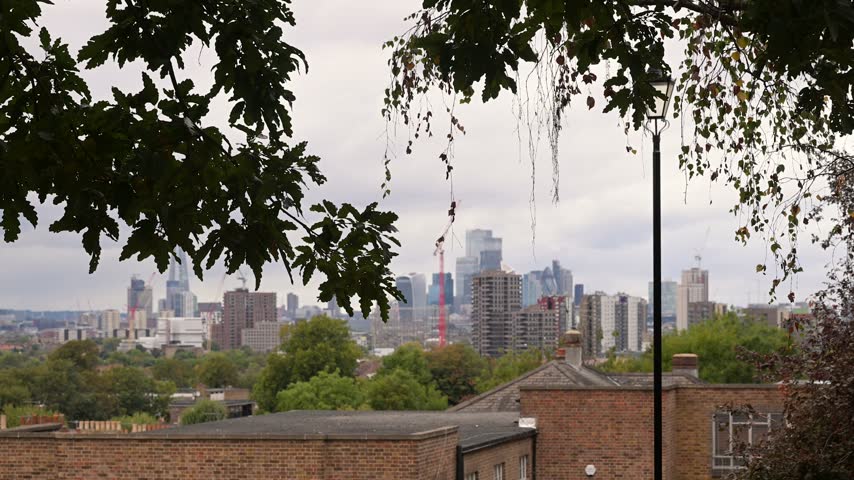 City skyscrapers sit in the distance beyond rooftops and green canopy from Telegraph Hill Park Upper Park viewpoint in New Cross.
