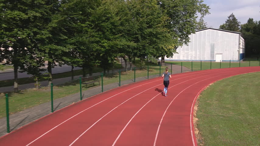 Woman running on track during outdoor workout. Back view of female runner training alone at stadium. Running, fitness and active lifestyle.