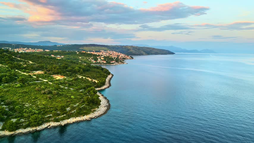 Aerial drone shot of coastal village Vrbnik on Krk island Croatia featuring rugged cliffs and calm blue sea at twilight.