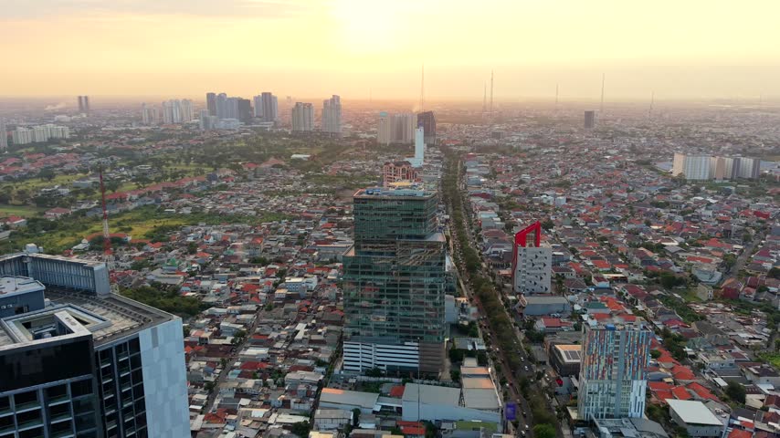 Aerial view of Surabaya, Indonesia at sunset, showing dense urban neighborhoods, modern high-rise buildings and city skyline in the warm evening light of East Java.