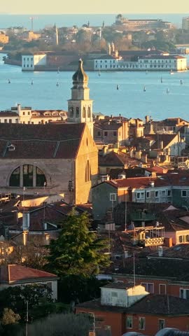 Aerial view over rooftops of Venice featuring church bell tower near water at sunset cinematic golden light footage.