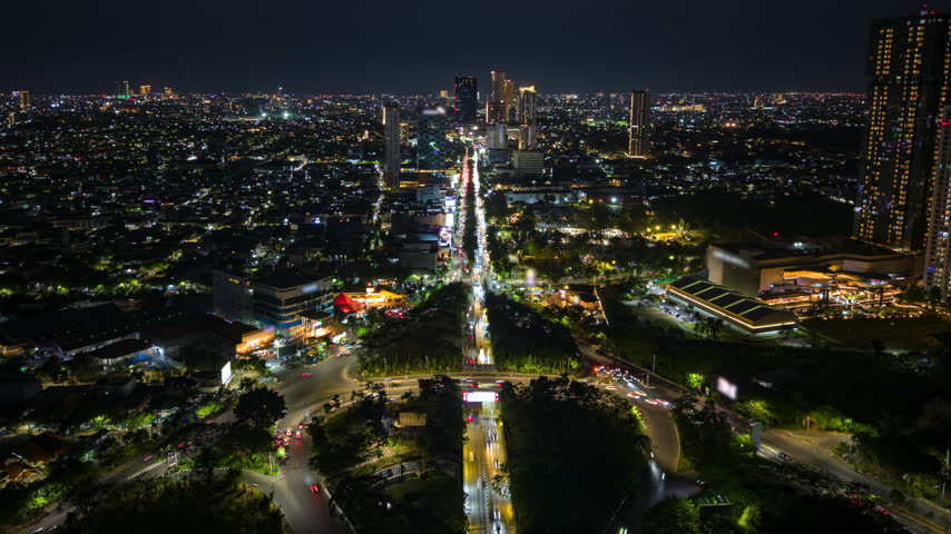 Aerial night timelapse of Surabaya, Indonesia, showing busy traffic along a major city road, illuminated buildings and an expansive urban skyline in East Java.