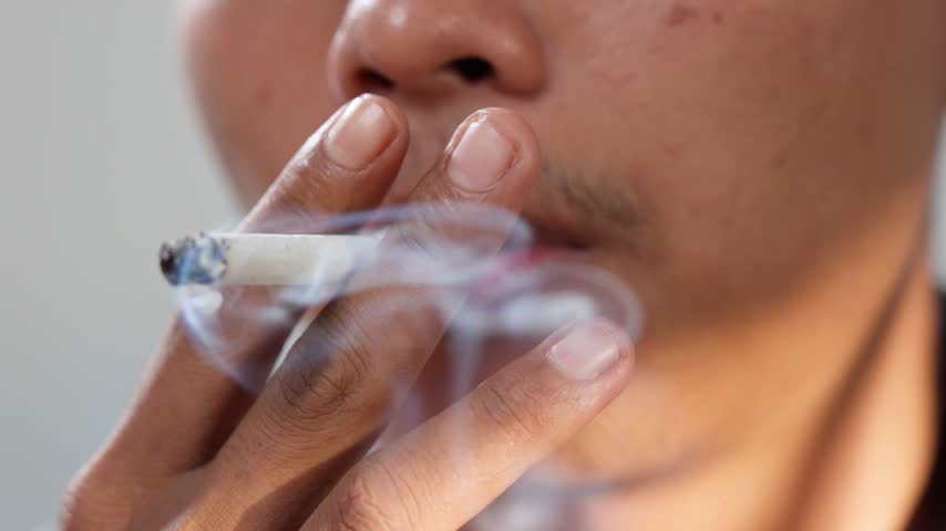 Close up of a young Asian man is smoking cigarette.