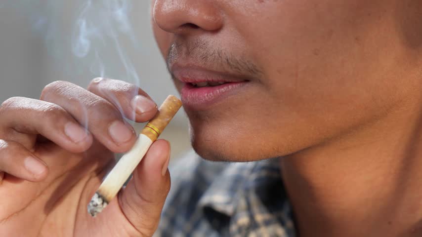 Close up of a young Asian man is smoking cigarette.