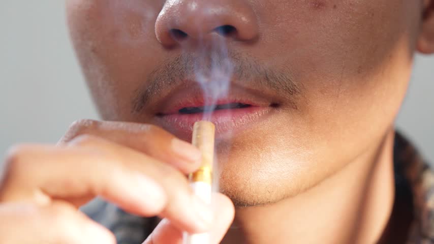 Close up of a young Asian man is smoking cigarette.
