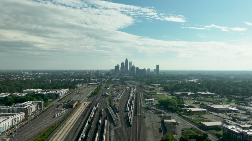 Drone hyper lapse footage of the Charlotte Skyline in North Carolina during early afternoon house over train tracks going backward with clouds on top during the summer
