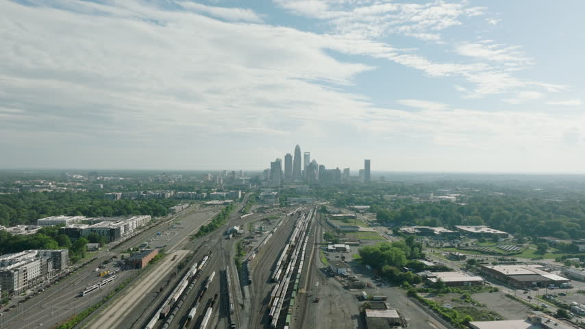 Drone footage of the Charlotte Skyline in North Carolina during early afternoon house over train tracks going backward with clouds on top during the summer