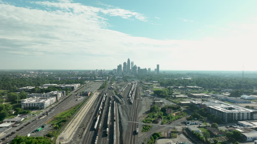 Drone hyper lapse footage of the Charlotte Skyline in North Carolina during early afternoon house over train tracks going forward with clouds on top during the summer