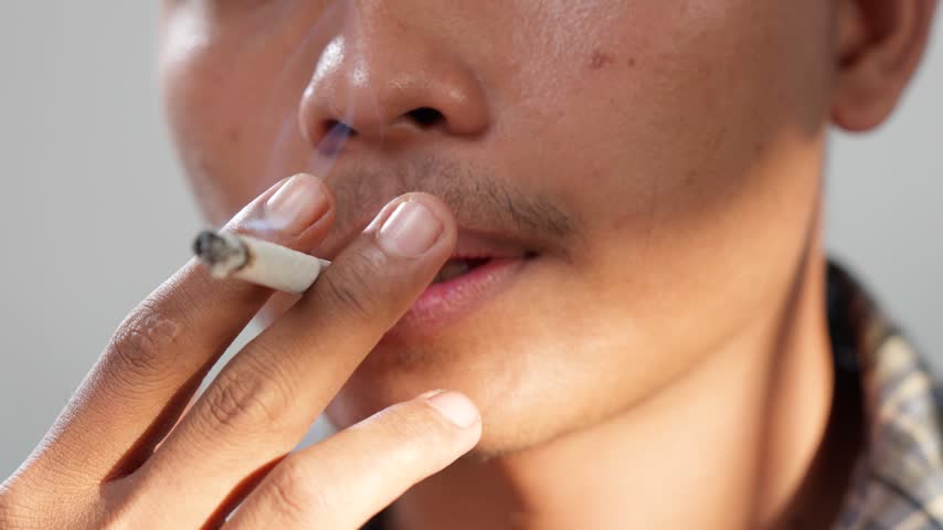 Close up of a young Asian man is smoking cigarette.