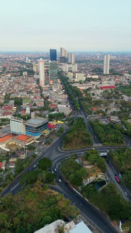 Aerial view of Surabaya, Indonesia, showing a large road intersection, traffic, dense urban neighborhoods and modern high-rise buildings across the East Java cityscape.