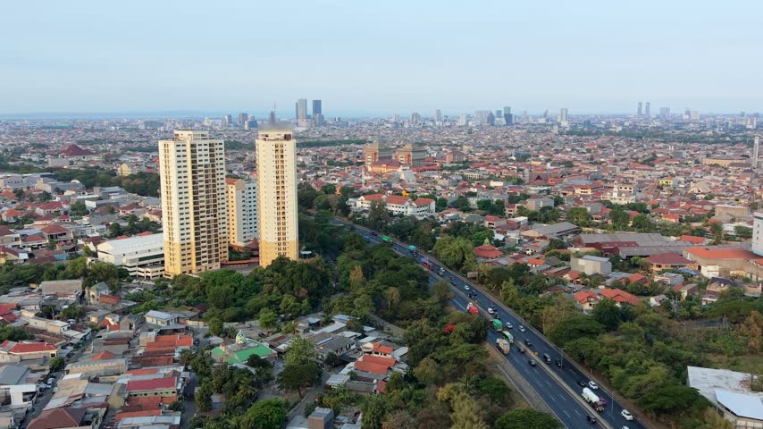 Aerial view of Surabaya, Indonesia, showing dense residential neighborhoods, high-rise buildings, a busy road and expansive city skyline across East Java.