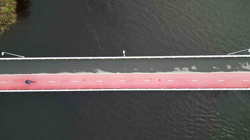 Aerial drone footage showcasing a modern pedestrian and bicycle bridge in Oulu, Finland, with active cyclists crossing the bridge.