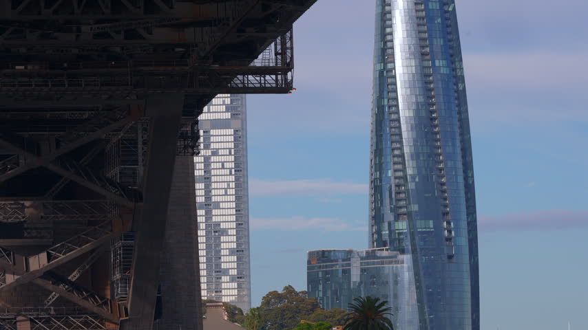 Contemporary glass skyscraper framed against the steel structure beneath the Sydney Harbour Bridge. Sydney, New South Wales, Australia.