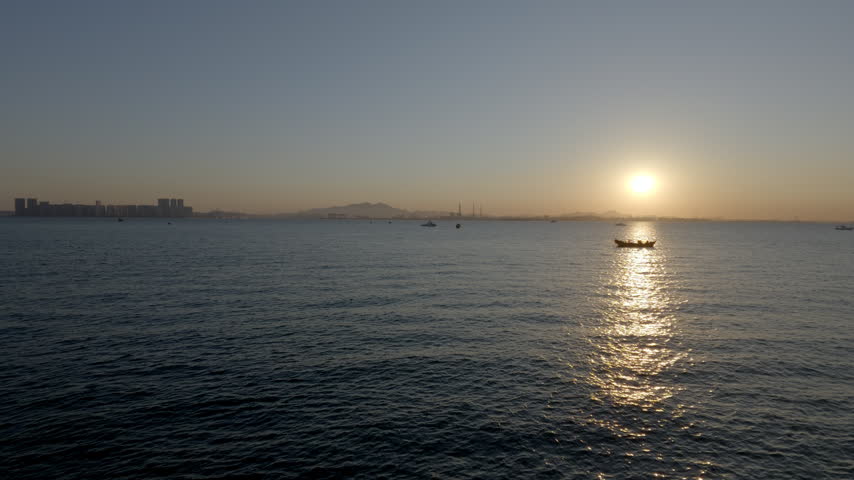 A serene seascape at sunset, with a small boat on calm water and a distant coastal skyline under a gradient sky.