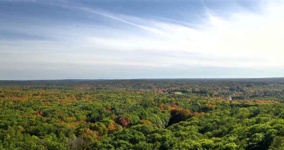 Drone flying up and over colorful fall foliage at Bradbury Mountain State Park, Maine with blue skies in the horizon.