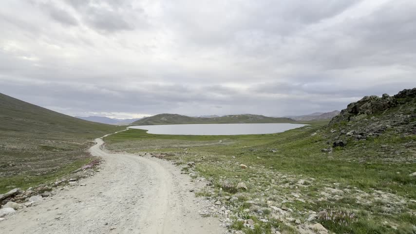 Unpaved road leads toward Sheosar Lake across an open highland plateau under cloudy skies