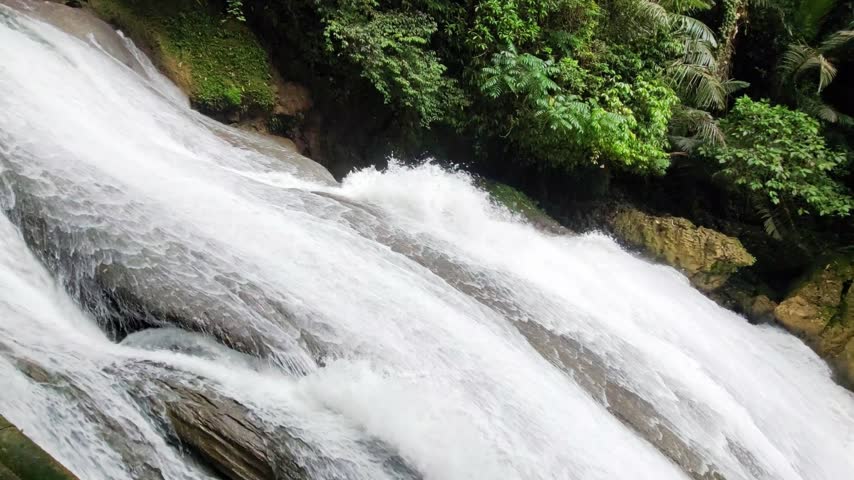 Close-up of fast water rushing down smooth rock slope in a tropical forest waterfall
