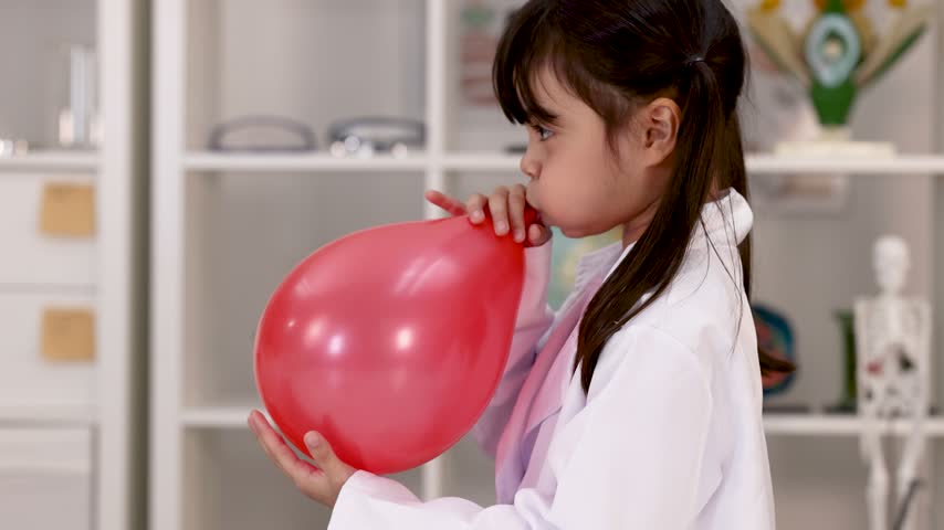 A young student in a white lab coat inflates a red balloon during STEM learning.