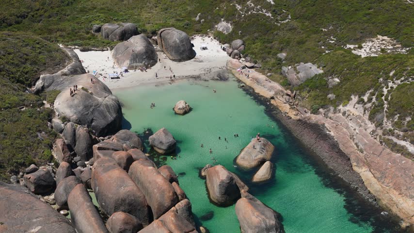 Aerial view of people swimming in a tranquil sheltered cove with calm turquoise waters enclosed by large rocks and vegetation