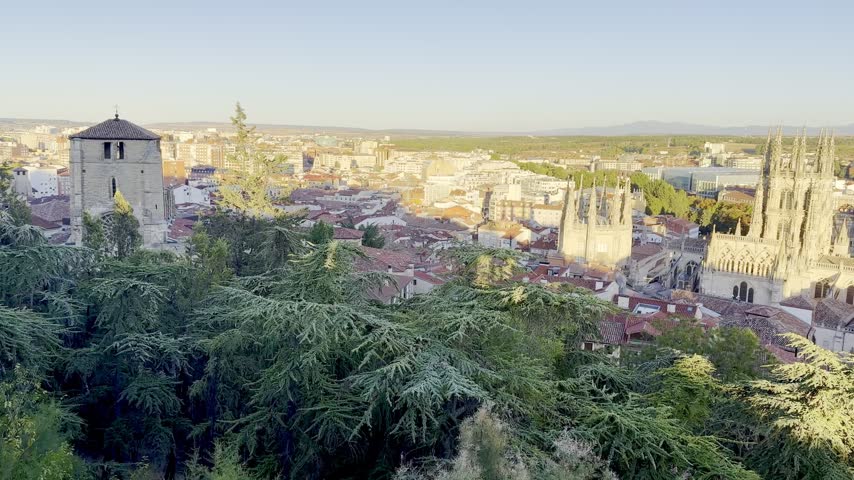 Wide elevated panorama of Burgos Cathedral, historic rooftops and the surrounding city illuminated by warm late afternoon light in Burgos, Spain.