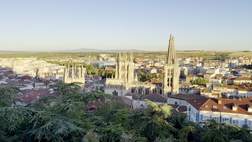 Scenic elevated view of the Gothic Burgos Cathedral dominating the historic rooftops and urban landscape of Burgos, Spain, in warm golden hour light.