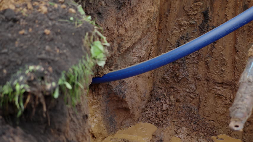 Thin blue plastic pipe hidden inside ground at construction site closeup. Plumbing utilities repair with modern supplies outdoors