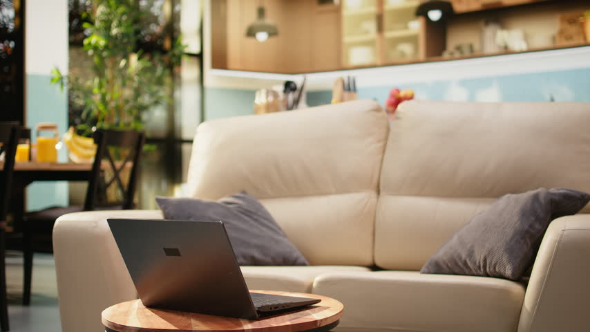 Living room interior features a laptop on a round coffee table, with warm tones, natural light, wooden furniture, a couch, and no people in the rustic home