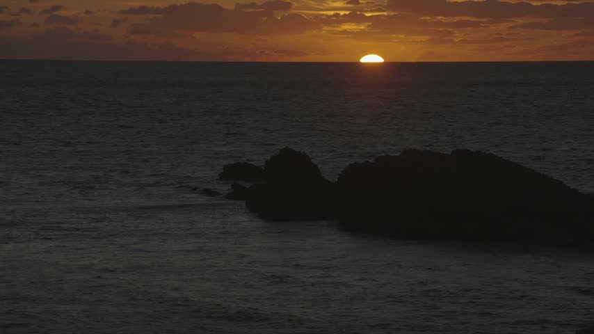 Close-up of a large rock as the sun disappears below the horizon at sunset