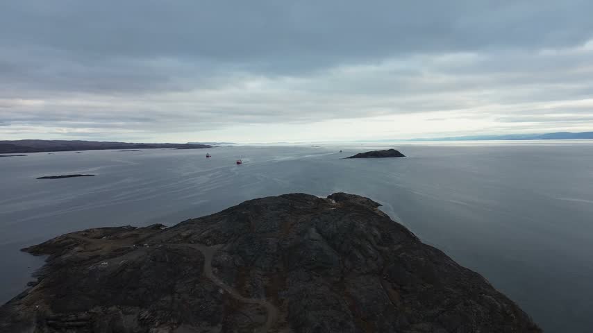 High elevation aerial drone flight over dark granite peninsula extending out into calm open ocean waters of Frobisher Bay near Iqaluit port