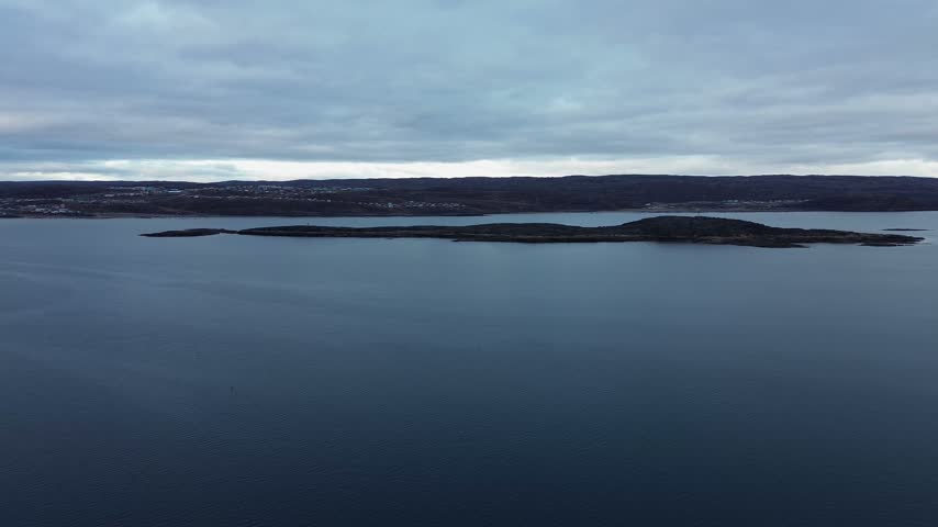 High elevation panoramic drone shot over dark blue waters of Frobisher Bay near Iqaluit shipping with distant tundra mainland in background